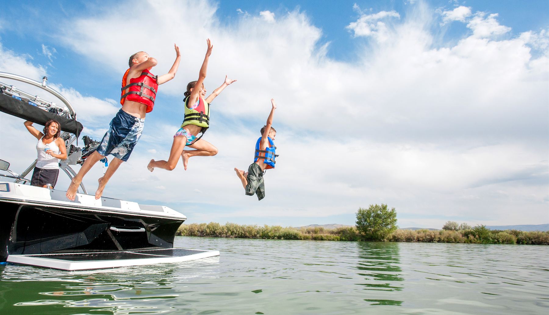 Kids in life jackets jumping from a boat into a lake