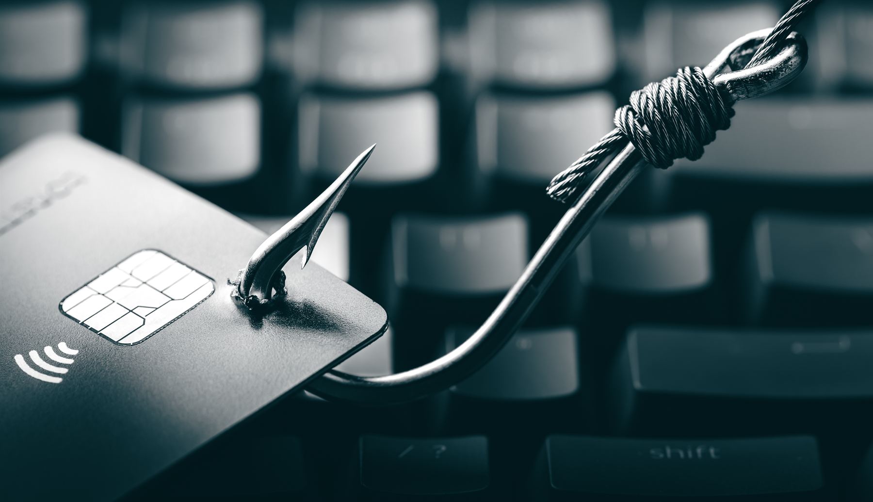 Credit card snagged on a fishing hook above a keyboard
