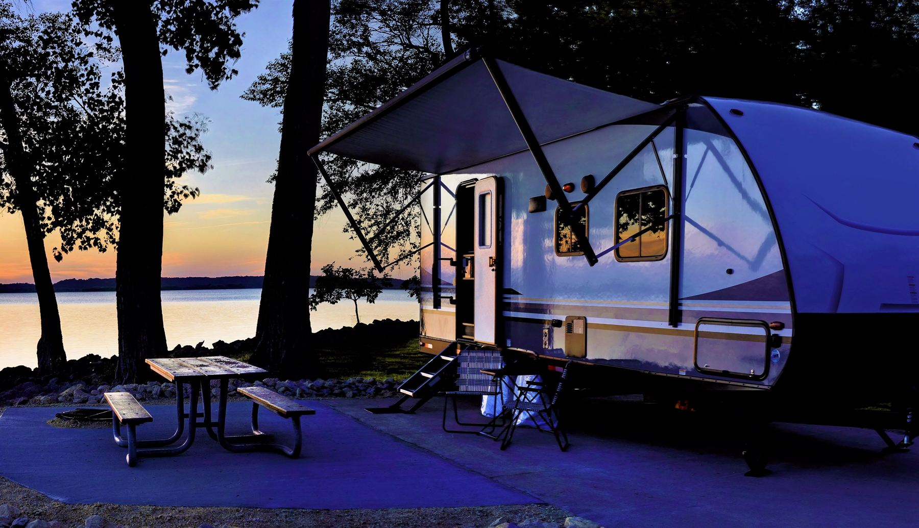 Travel trailer parked at a lakeside campsite at sunset